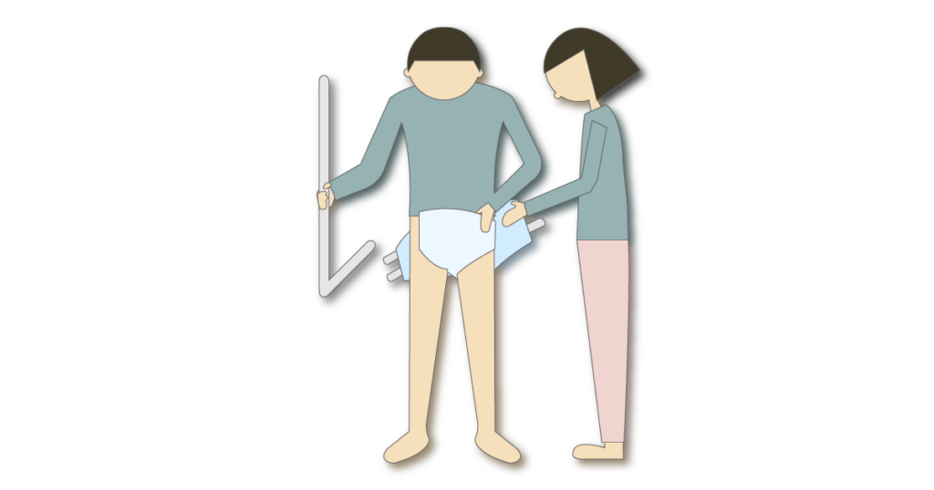 L字手すりにつかまった方の立位で、介助者がテープ型おむつを交換する様子